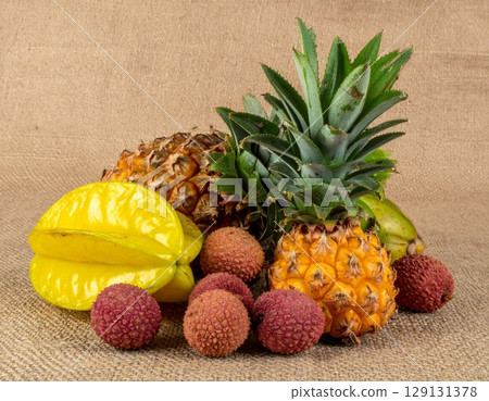 Bright Still Life Featuring Pineapple Starfruit and Lychee on Burlap Background 129131378