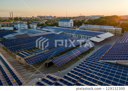 Aerial view of solar power plant with blue photovoltaic panels mounted on industrial building roof for producing green ecological electricity at sunset. Production of sustainable energy concept Aerial view of solar power plant with blue photovoltaic panels mounted on industrial building roof for producing green ecological electricity at sunset. Production of sustainable energy concept 129132300