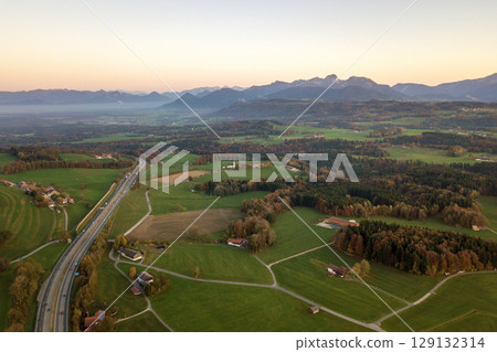 Aerial view of small scattered farm houses with red tiled roofs among green farming fields and distant mountain forest in summer. Aerial view of small scattered farm houses with red tiled roofs among green farming fields and distant mountain forest in summer. 129132314