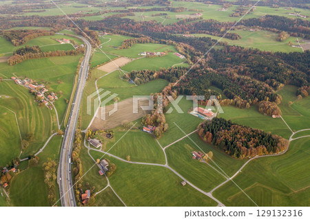 Aerial view of small scattered farm houses with red tiled roofs among green farming fields and distant forest in summer. Aerial view of small scattered farm houses with red tiled roofs among green farming fields and distant forest in summer. 129132316