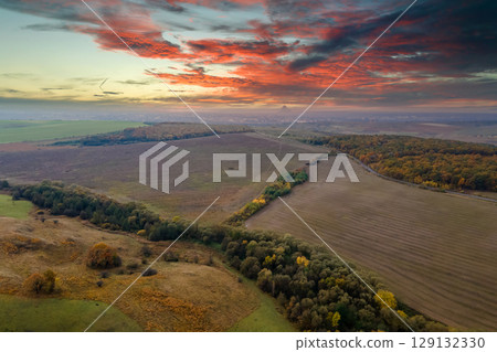 Aerial view of plowed agricultural fields with cultivated fertile soil prepared for planting crops between green woods in fall season Aerial view of plowed agricultural fields with cultivated fertile soil prepared for planting crops between green woods in fall season 129132330