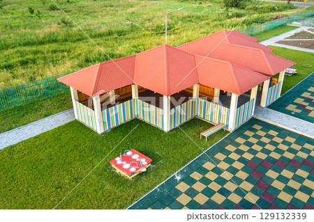 Aerial view of new alcove in kindergarten play yard with red tiled roof for outdoor children activities. Aerial view of new alcove in kindergarten play yard with red tiled roof for outdoor children activities. 129132339