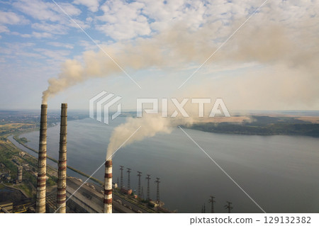 Aerial view of high chimney pipes with grey smoke from coal power plant. Production of electricity with fossil fuel. 129132382