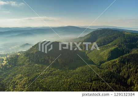 Aerial view of green mountain hills covered with evergreen spruce forest in summer. 129132384
