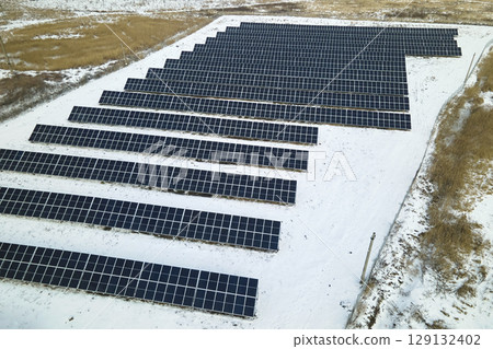Aerial view of electrical power plant with solar panels covered with snow melting down in winter end for producing clean energy. Concept of low effectivity of renewable electricity in northern region Aerial view of electrical power plant with solar panels covered with snow melting down in winter end for producing clean energy. Concept of low effectivity of renewable electricity in northern region 129132402
