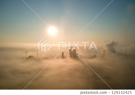 Aerial view of cement factory with high concrete plant structure and tower crane at industrial production site on foggy morning. Manufacture and global industry concept. 129132425