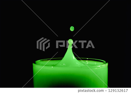 A water drop creating a splash in a green-colored liquid. 129132617