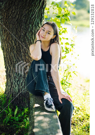 Serene student enjoying a tranquil moment in nature, surrounded by lush greenery and embracing the peacefulness of the outdoors 129132818