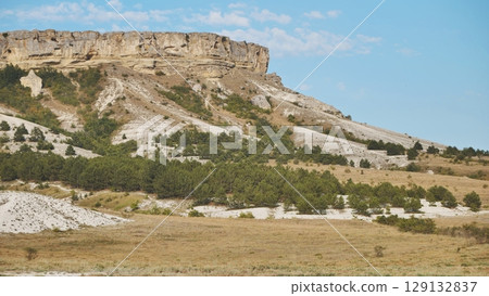 White rocky mountain rising through verdant forest, green slopes contrasting against vivid azure sky 129132837