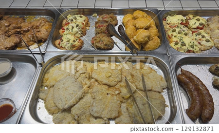 Metal trays containing various types of meat dishes ready to be served in a self-service restaurant 129132871