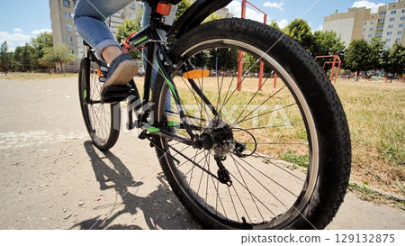 Low angle view of rear bicycle wheel with school girl riding bicycle in urban park during summer day 129132875