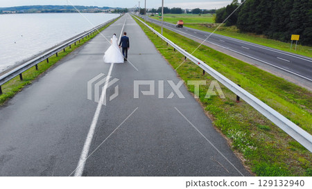 Newlyweds on their wedding day walk along the road. Drone view. 129132940