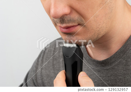 Man grooming his facial hair with electric trimmer in well-lit indoor space 129132957
