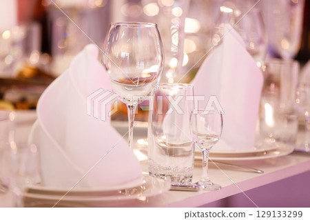 Empty glass set in restaurant. wedding, decor, celebration, holiday concept - romantic table setting with white tablecloth, plates, crystal glasses 129133299