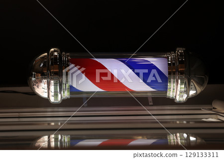 Barber pole spinning at night. International barbershop pole sign. A barber pole calling for people at street. Vintage barbershop. Salon. Barber pole spinning at night. International barbershop pole sign. A barber pole calling for people at street. Vintage barbershop. Salon. 129133311