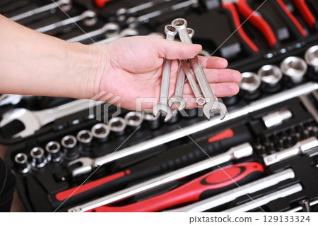 Tool store. Closeup of male hand holding wrenches. Auto repair kit in toolbox. Repairman instruments set. Inside the toolbox there are black-red wrenches, spanners and different nozzles. Closeup. 129133324