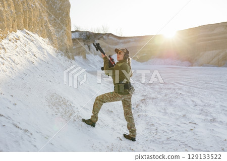 Female soldier climbing snowy hill holding rifle during sunset 129133522