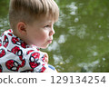 Small boy playing on a pond handsome teenager boy launches kite on the sea in blue sky, close up. High quality photo 129134254