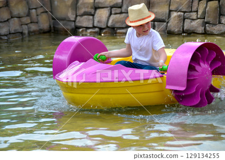 Kid playing rowing water paddle boat. Soft focus. A little girl rides a colorful boat on a pool in a resort. High quality photo Kid playing rowing water paddle boat. Soft focus. A little girl rides a colorful boat on a pool in a resort. High quality photo 129134255