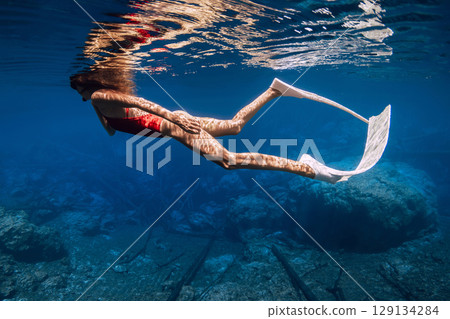 Freediver woman with diving fins swims in transparent lake in sunny day Freediver woman with diving fins swims in transparent lake in sunny day 129134284
