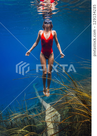 Beautiful woman swims underwater in blue lake. 129134285