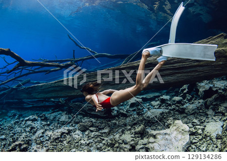 Freediver woman dives underwater with fins in the lake with sunken logs. 129134286