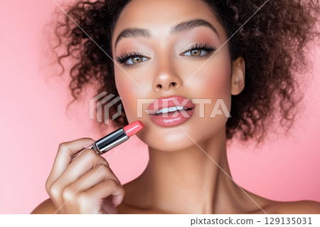Beauty portrait of a well-groomed woman applying lipstick to her lips on a pink background 129135031