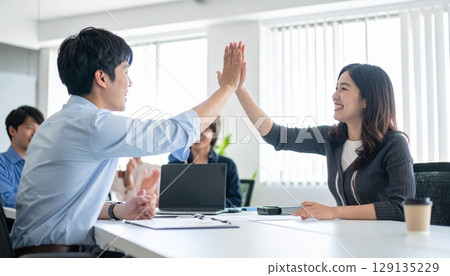Business people high-fiving in a bright office 129135229