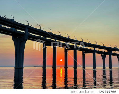 Scenic sunset over the sea. The sun setting between the pillars of the bridge. Reflection of sunlight on water. The sky is painted in golden colors. Kanonersky Island, Saint-Petersburg 129135766