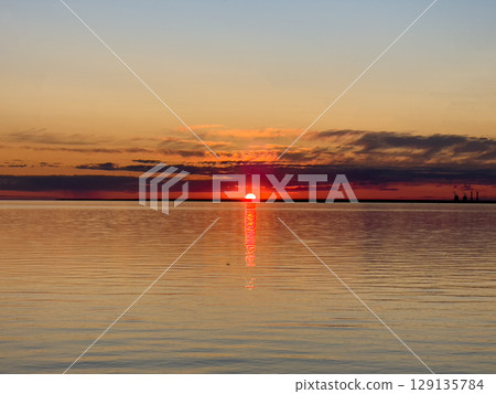 Beautiful sunset over the sea. The sun sets on the water. The sky is painted with bright colors. Summer evening. Sunset beach. 129135784