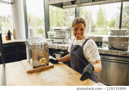 A Cheerful Baker Smiling in a Modern Kitchen While Using a Pasta Maker for Culinary Art A Cheerful Baker Smiling in a Modern Kitchen While Using a Pasta Maker for Culinary Art 129135909