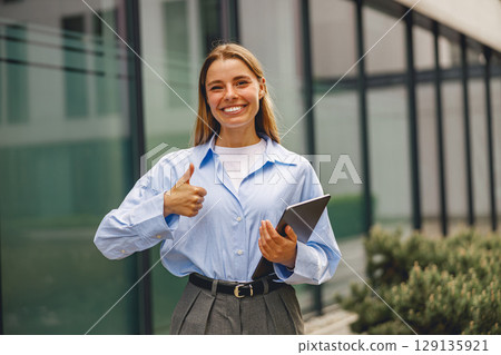 A Professional Woman Smiling Cheerfully Outdoors While Holding a Tablet Device in Her Hands A Professional Woman Smiling Cheerfully Outdoors While Holding a Tablet Device in Her Hands 129135921
