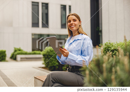 A cheerful and smiling businesswoman is using a tablet in a vibrant modern urban environment A cheerful and smiling businesswoman is using a tablet in a vibrant modern urban environment 129135944