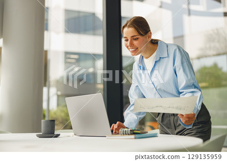 A Professional Woman Engaged in Work on a Laptop in a Modern, Bright, Stylish Office Environment 129135959