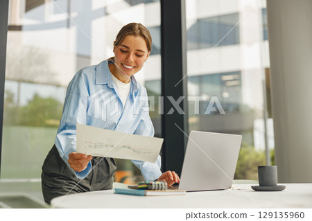 A successful businesswoman reviews reports in a modern office, showing her commitment to excellence A successful businesswoman reviews reports in a modern office, showing her commitment to excellence 129135960