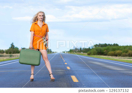 Blonde woman with a green retro suitcase standing on the highway. Blonde woman with a green retro suitcase standing on the highway. 129137132