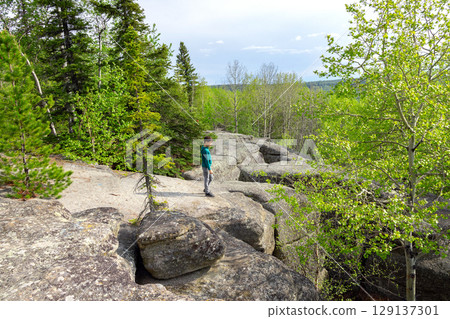 Boy is hiking in the prehistoric Rock formation in the green forest. 129137301