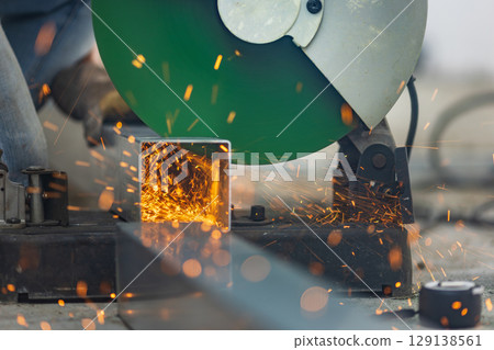 Worker cutting steel rectangular pipe in construction site. 129138561