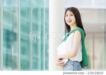 Smiling female college student with laptop in university hallway 129138635