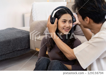 Young Couple Enjoying Music Together at Home with Headphones in a Cozy Living Room Setting Young Couple Enjoying Music Together at Home with Headphones in a Cozy Living Room Setting 129138794