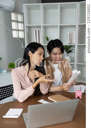 Young Couple Reviewing Finances at Home with Laptop and Piggy Bank for Smart Money Management and Budget Planning Young Couple Reviewing Finances at Home with Laptop and Piggy Bank for Smart Money Management and Budget Planning 129138802