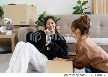 Young Women Enjoying a Break While Unpacking in New Home Surrounded by Moving Boxes and Cozy Furniture in a Bright Living Room Setting 129138817