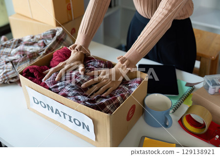 Hands Organizing Clothes in Donation Box for Charity and Community Support Hands Organizing Clothes in Donation Box for Charity and Community Support 129138921