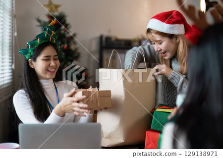 Joyful Christmas Celebration with Friends Exchanging Gifts by the Christmas Tree in a Cozy Living Room Setting 129138971