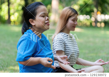 Two Women Meditating Outdoors in a Peaceful Park Setting, Practicing Mindfulness and Relaxation in Nature, Embracing Tranquility and Inner Peace 129138972