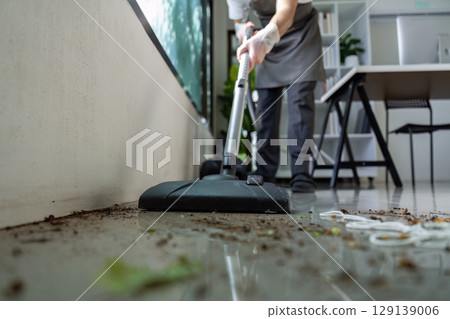 Professional Cleaner Using Vacuum to Remove Dirt from Modern Office Floor with Efficient Cleaning Techniques 129139006