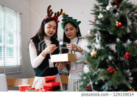 Two Women Decorating a Christmas Tree with Festive Headbands and Gift Box in a Bright Living Room Setting Two Women Decorating a Christmas Tree with Festive Headbands and Gift Box in a Bright Living Room Setting 129139014