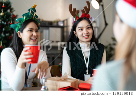 Festive Office Celebration with Colleagues Wearing Holiday Accessories and Enjoying Drinks in a Decorated Workspace 129139018