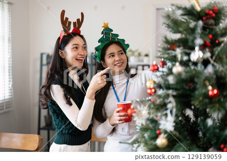 Festive Friends Decorating Christmas Tree with Joyful Holiday Spirit and Cheerful Smiles in Cozy Living Room Setting 129139059