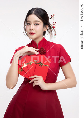 Portrait of joyful beauty Asian woman in red Cheongsam Chinese traditional dress celebrating with lucky red envelopes on Chinese New Year festival isolated on white background. 129139079